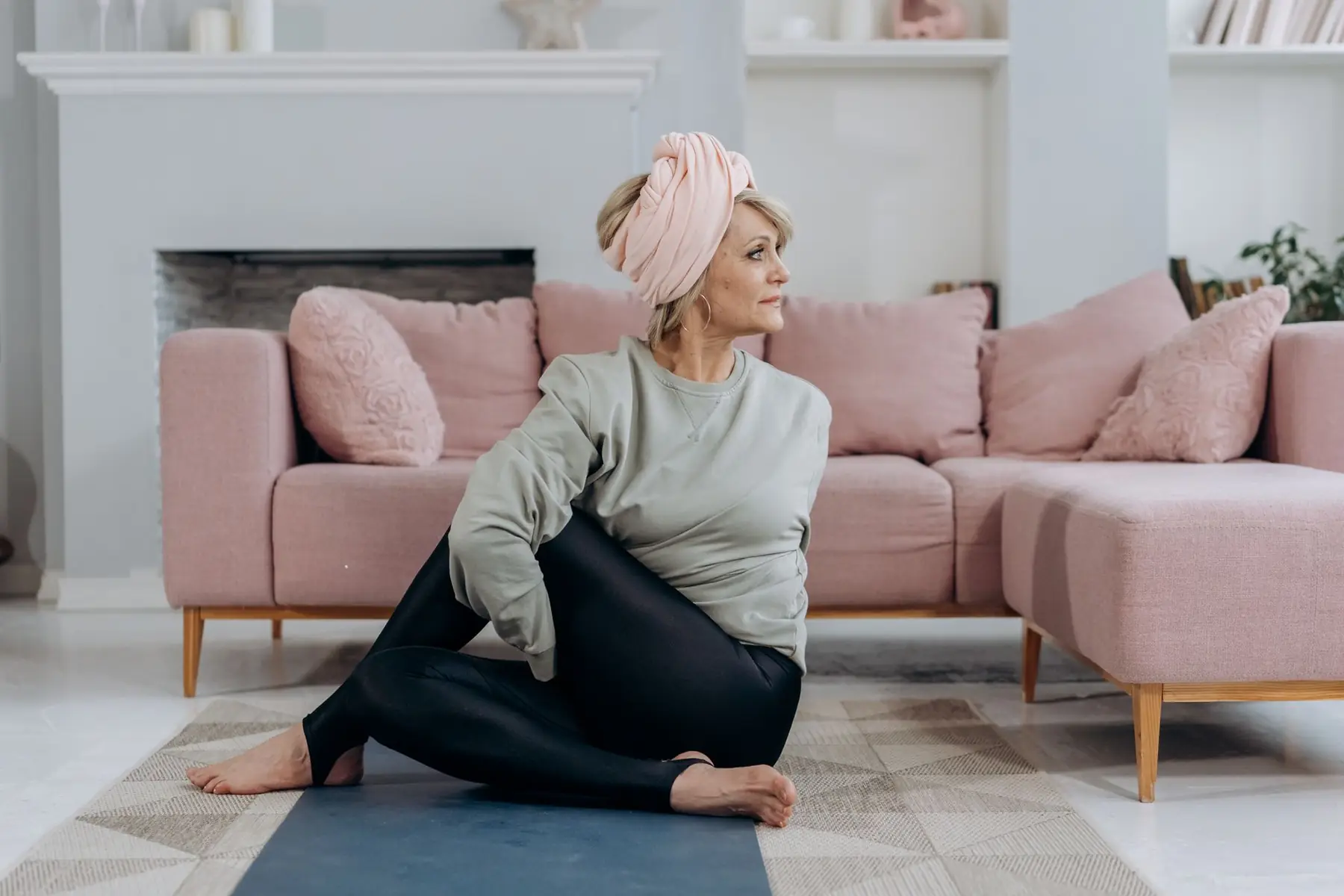 Full body of middle aged woman in sportswear and headband sitting on mat while