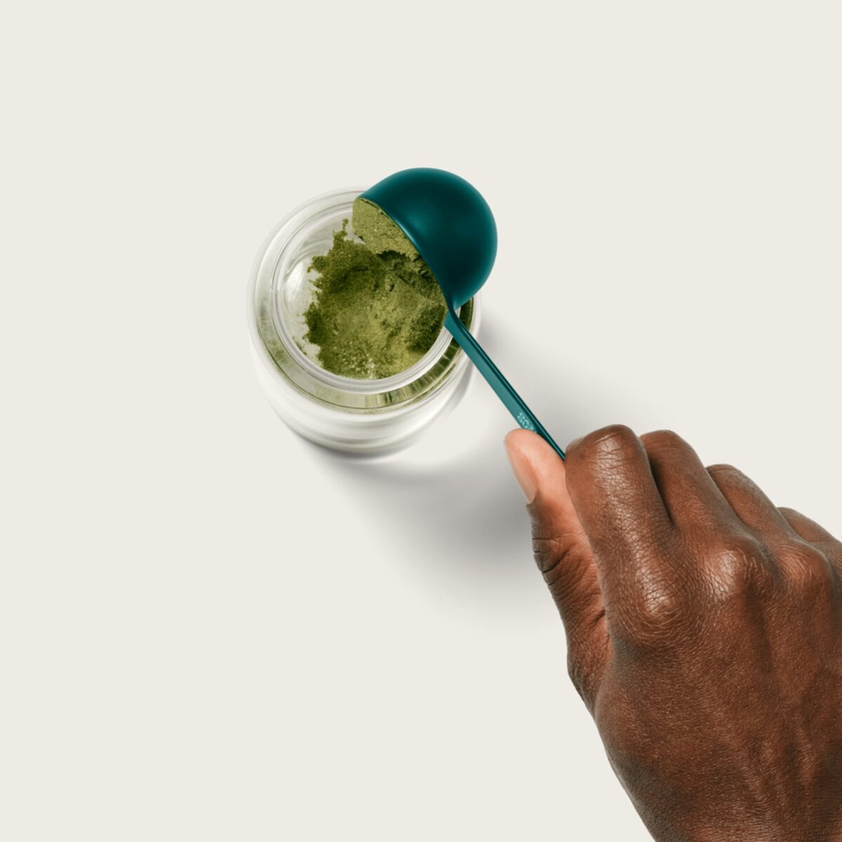 A hand scooping AG1 powder into a glass